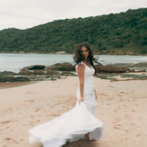 Elegant bride in white dress on sandy beach with ocean view. Captured with natural ambiance.