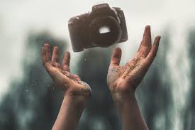 pair of hands tossing a DSLR camera into the air, with a blurred background of trees and sky, suggesting creativity or freedom in photography.